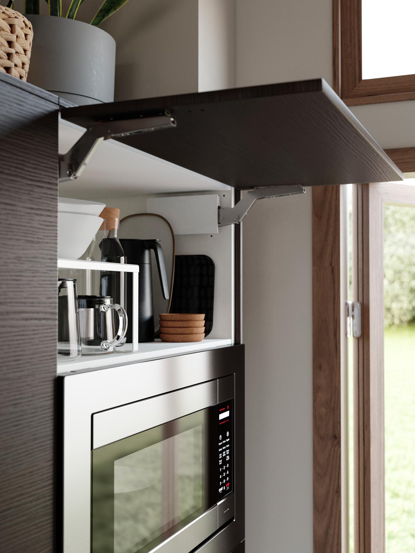 An ASKERSUND kitchen in dark brown with a HUVUDSAKLIG microwave, a cabinet is open revealing bowls and coffee accessories.