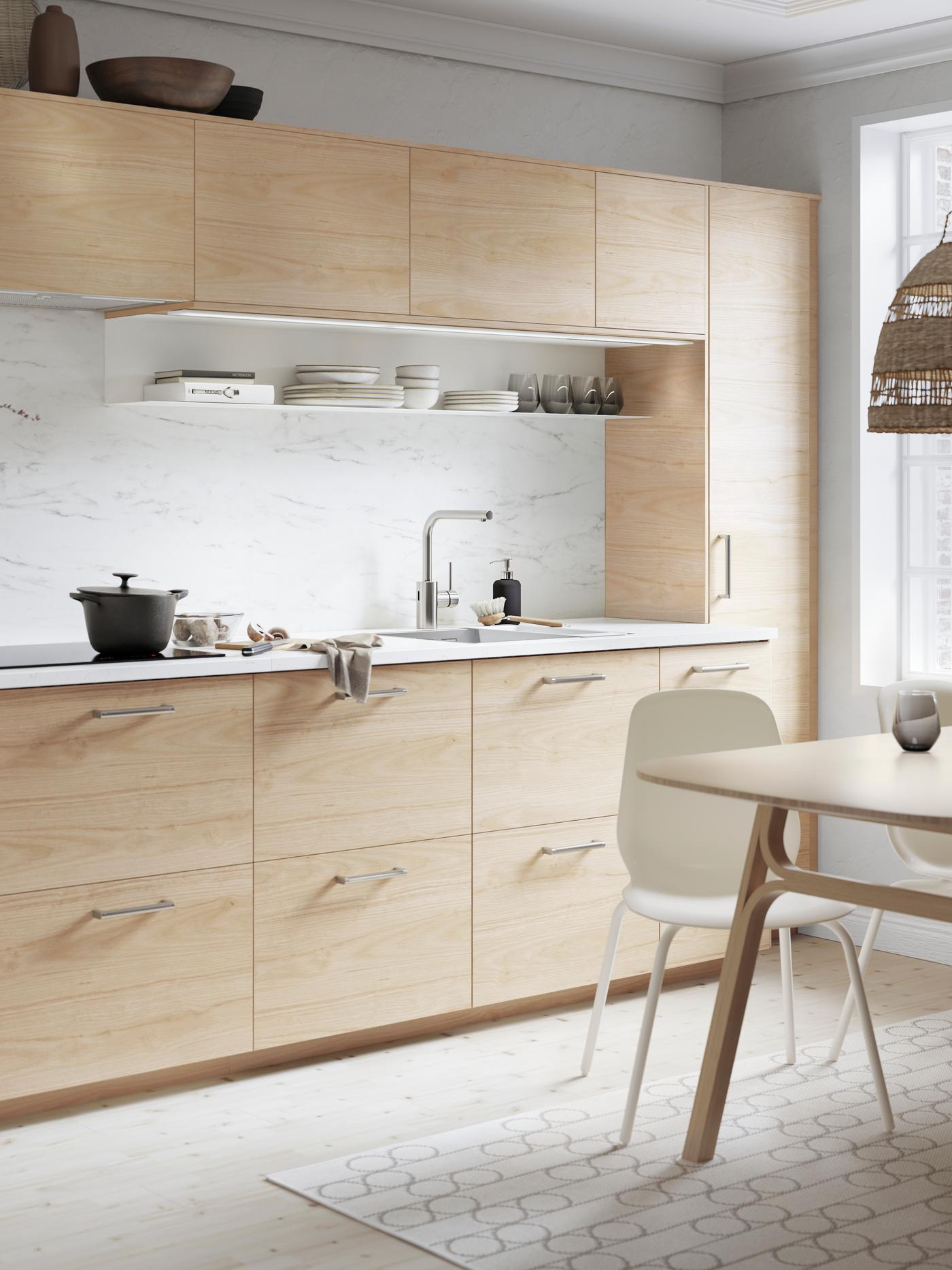 An ASKERSUND kitchen in light ash effect with an EKBACKEN worktop in white marble effect. There is a frying pan on the hob.