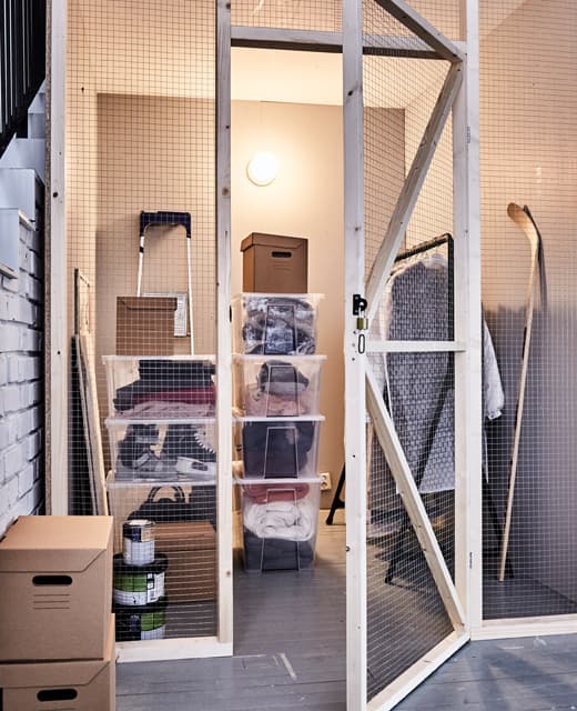 An attic space stores winter items in stackable, clear plastic boxes, paper boxes and a clothing rack.
