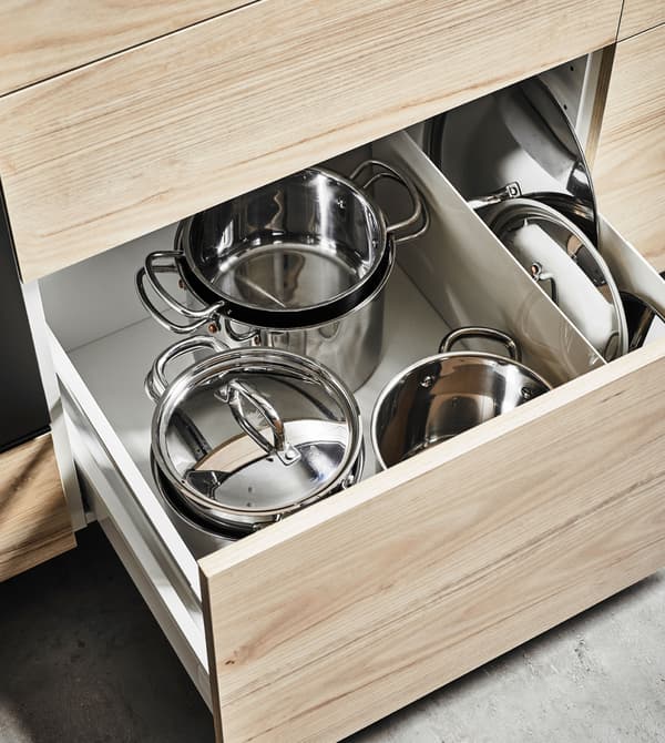An deep kitchen drawer with an ash front that’s open to show organised pots and lids 