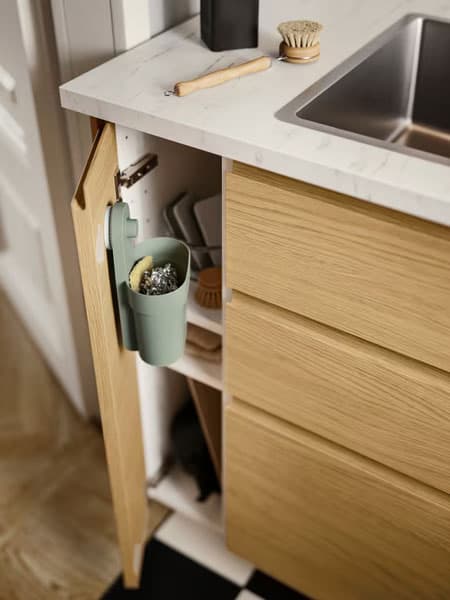 An der Innenseite einer VOXTORP Schranktür in Eichenachbildung hängt ein graugrüner ÖBONÄS Behälter mit Saugnapf.