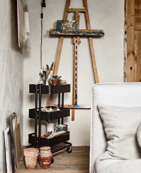 An easel hung on a wall, and a trolley with art supplies next to it.