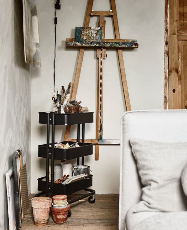 An easel is hung on a wall, while a trolley next to it holds art supplies.