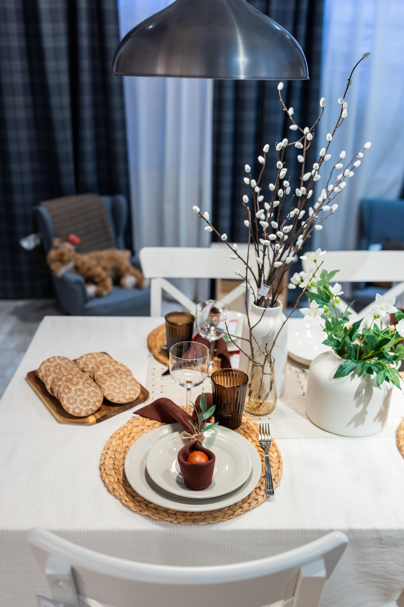 An Easter table setting in white and beige, with vases of flowers and willows on the table.