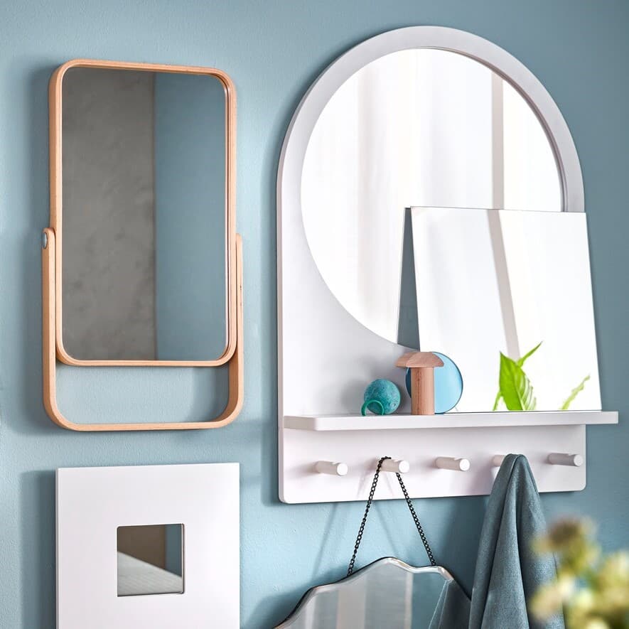 An einer blauen Wand hängen 2 Spiegel und hacken darunter für Handtücher. Vor dem Spiegel stehen kleine Dekoartikel.