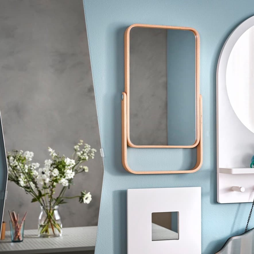 An einer hellblauen Wand hängt ein Spiegel. Auf der linken Seite kann man eine Vase mit einer Pflanze sehen.