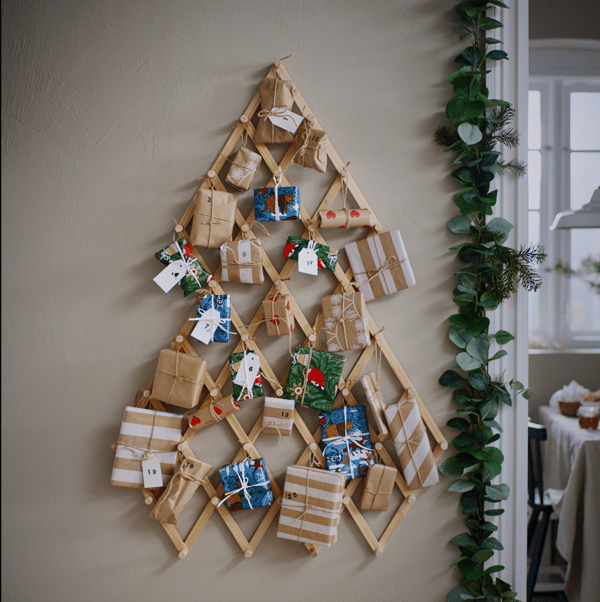 An einer Wand hängt ein Holzgestell das aussieht wie ein Baum und daran hängen kleine Geschenke.