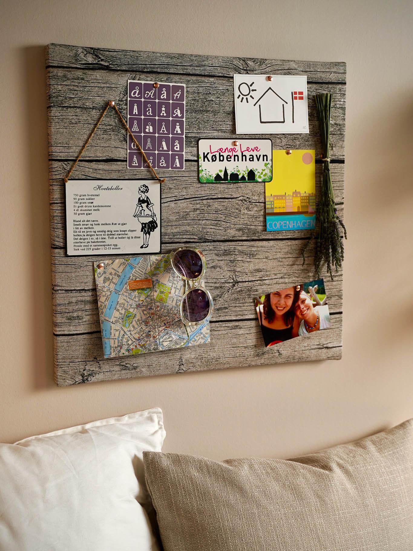 An einer Wand hängt ein Holzschild mit Bilder und Texten darauf über einem Sofa.