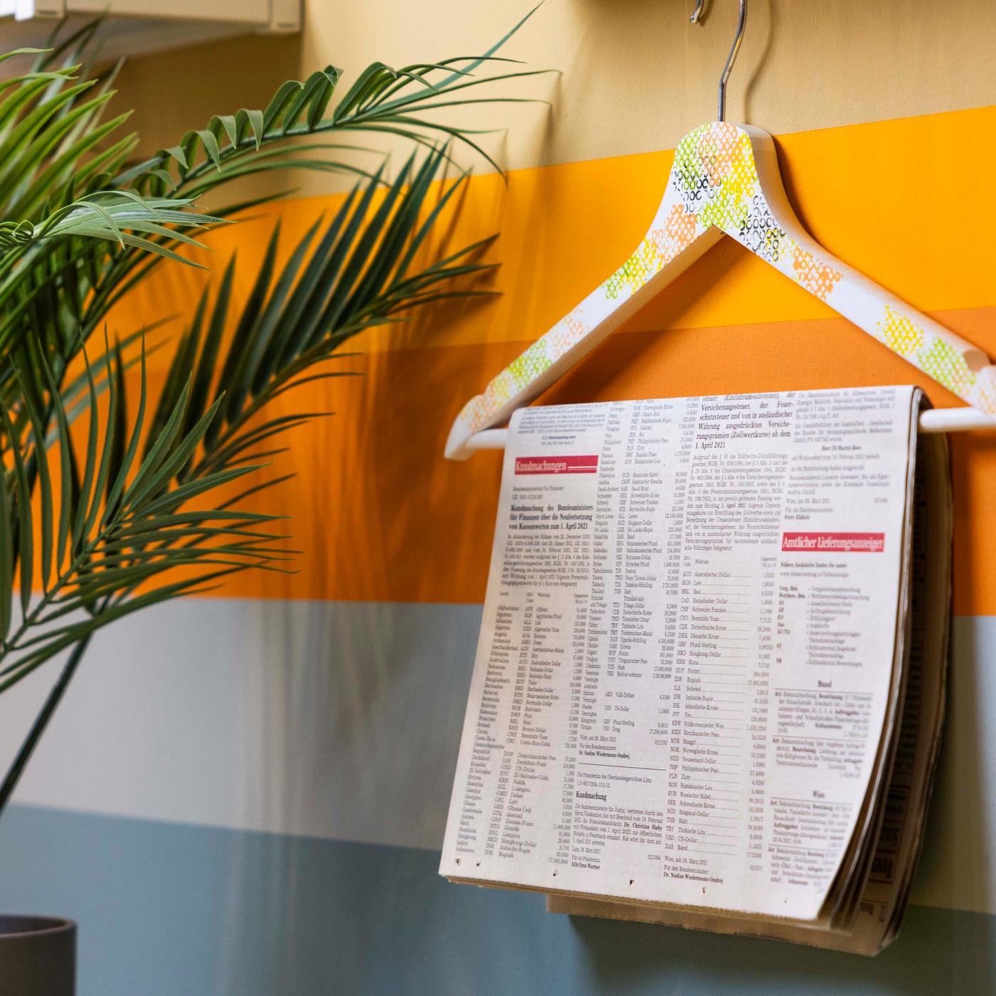 An einer Wand hängt ein Kleiderbügel und daran ein weißer Zettel mit einer Schrift.