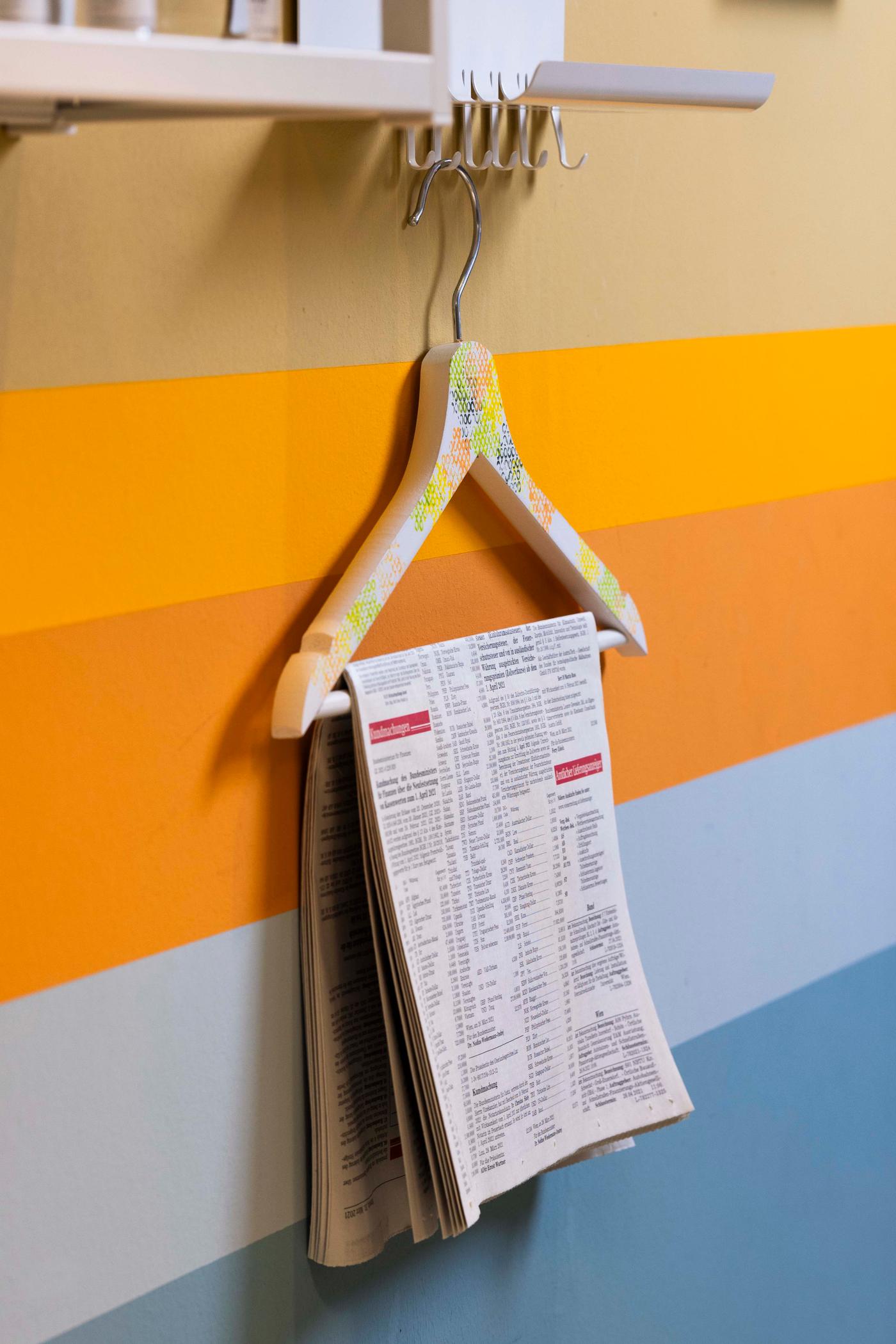 An einer Wand hängt ein Kleiderbügel und daran ein weißer Zettel mit einer Schrift.