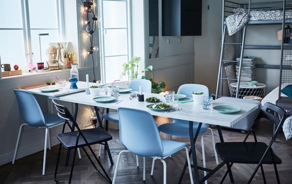 An EKBACKEN work top with white marble effect used as a pop-up table top surrounded by stackable and foldable chairs.