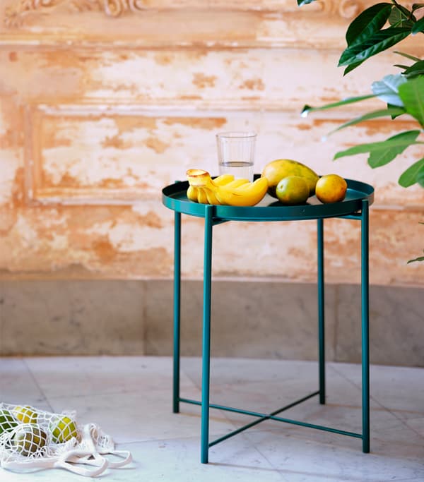 An emerald green tray table bearing various fruits, standing on a tiled surface.
