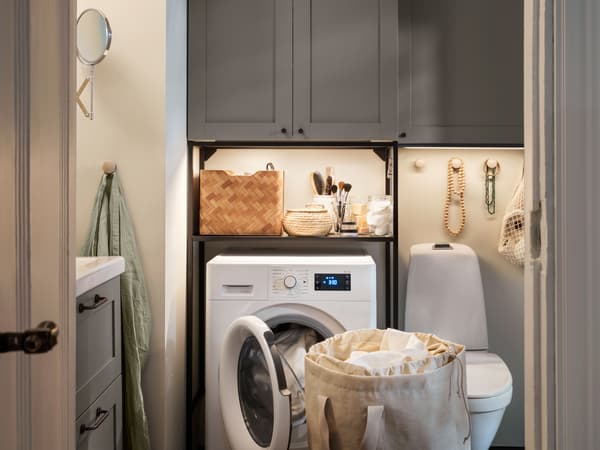 An ENHET laundry solution in grey with closed cabinets and a frame around the washing machine, placed in a small bathroom.