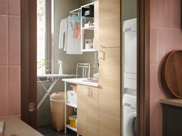 An ENHET laundry solution in white frames and oak doors with open shelves filled with washing powder and storage boxes.