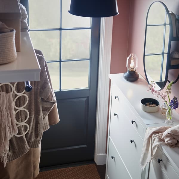 An entryway with side-by-side white HEMNES two-compartment shoe cabinets, clothing, and accessories on a multi-use hanger.