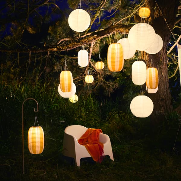 An evening garden with a white chair and plenty of hanging white and orange solar-powered SOLVINDEN pendant lamps. 