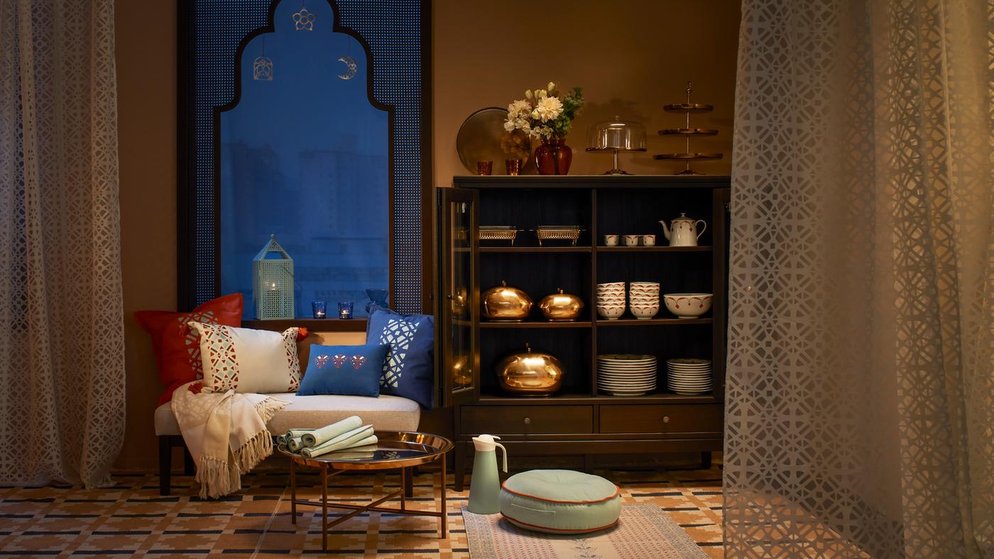 An evening scene showing the GOKVÄLLÅ collection of home accessories arranged on a sofa, coffee table and set of shelves.