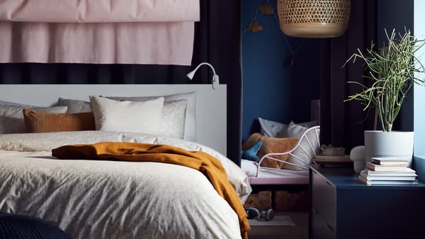 An extendable bed by a white bed with beige/white bed linen, a dark beige cushion, pink curtains and a bamboo pendant lamp.