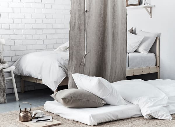 An extra sleeping space is made by placing a mattress on the bedroom floor next to a curtain that’s a room divider.