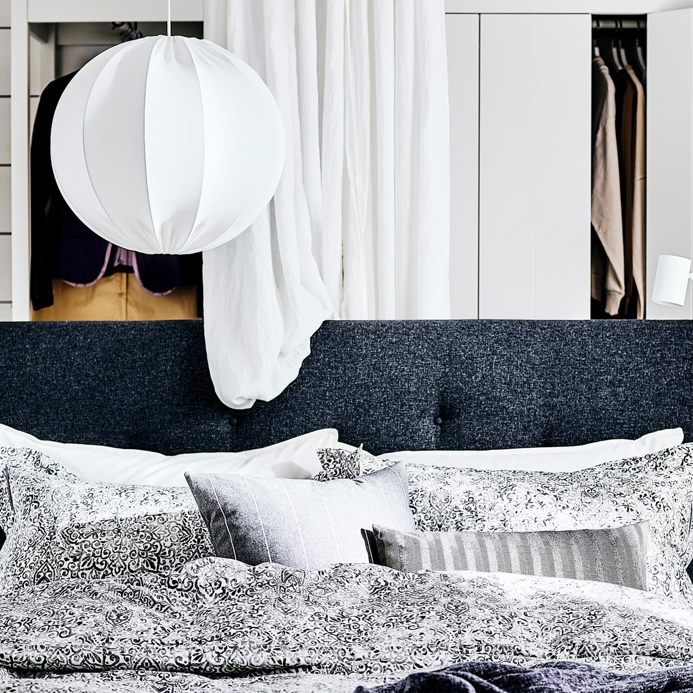 An IDANÄS upholstered bed frame with a black and white graphic duvet cover in front of a white IDANÄS open wardrobe.