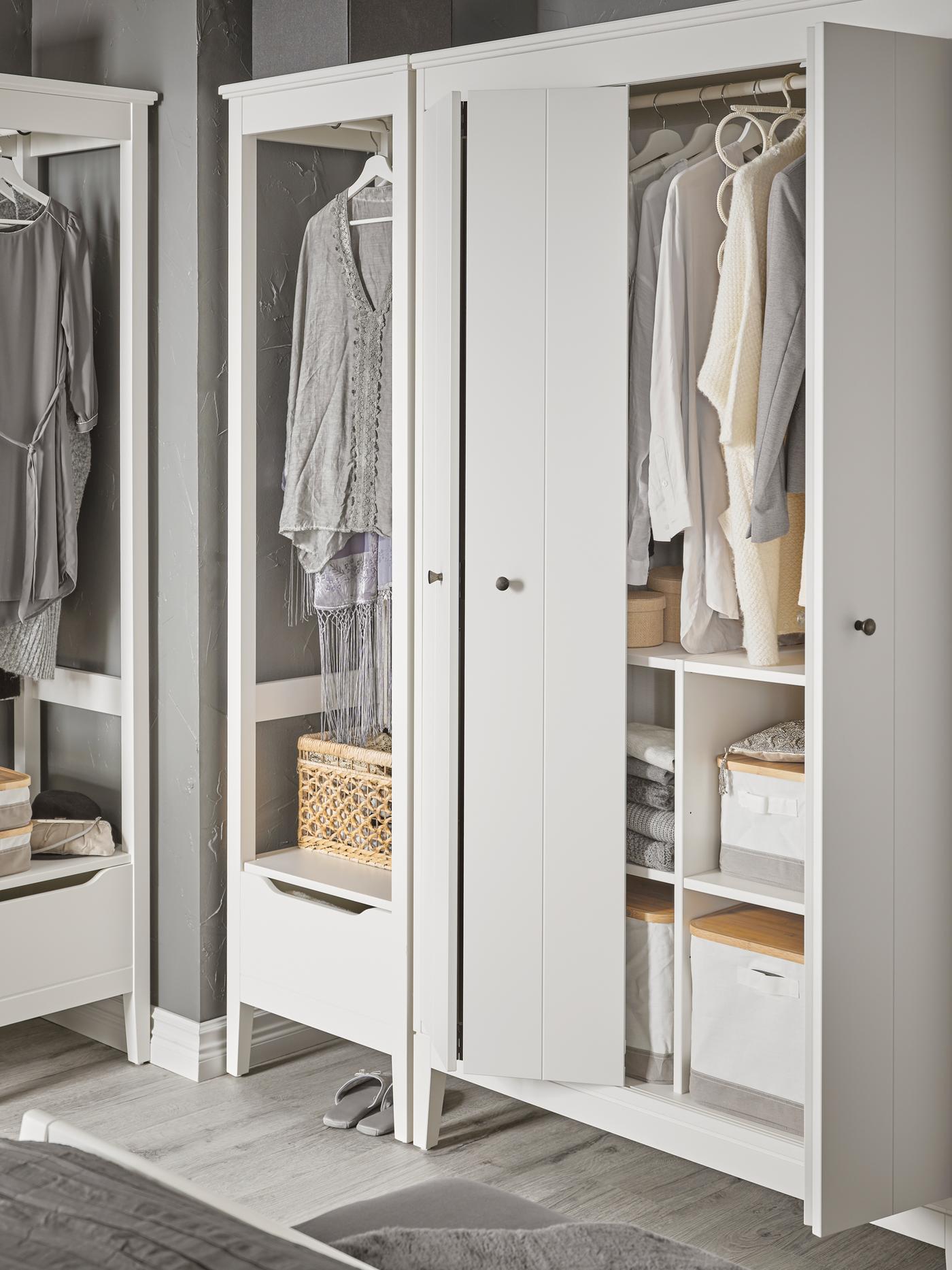 An IDANÄS wardrobe combination including an open wardrobe stands in a corner. One door is open: boxes and clothes are inside.