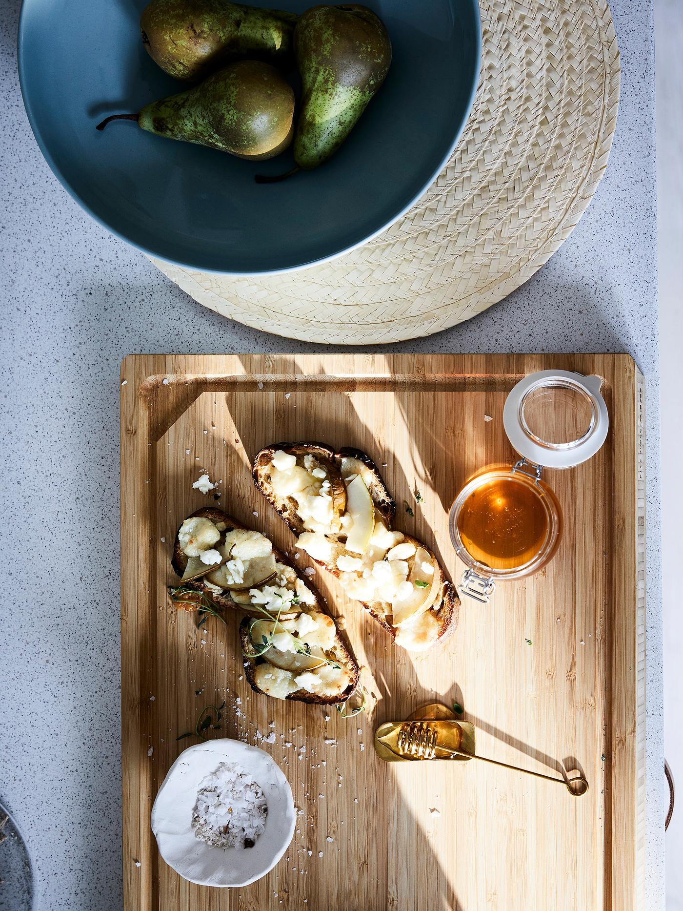 An IKEA APTIGLIG butcher’s block presenting food, a SLUTEN placemat made from palm leaves and a blue bowl with pears.