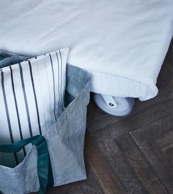An IKEA bag holding bedding for guests, next to a white sofa bed.