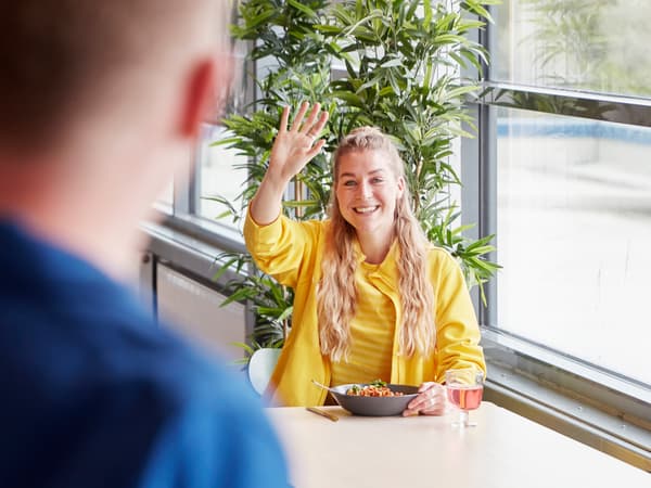 An IKEA co-worker dressed in a yellow uniform waving to a colleague in the staff canteen.