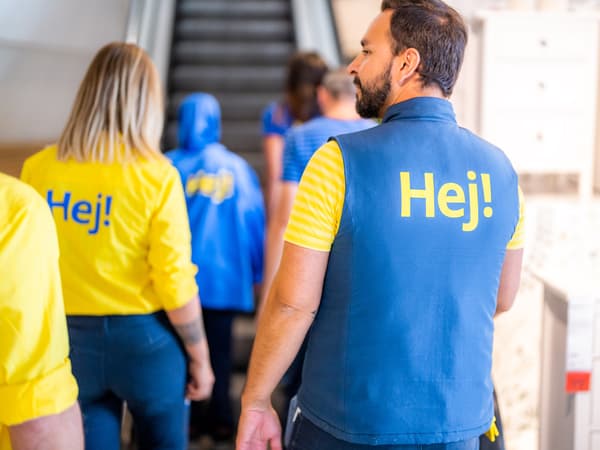 An IKEA co-worker dressed in a yellow uniform waving to a colleague in the staff canteen.
