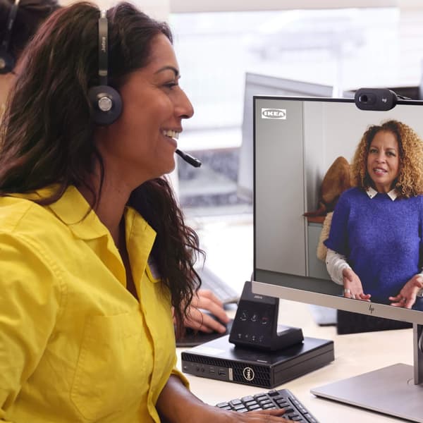 An IKEA co-worker has a headset on with a yellow shirt and is speaking to a customer virtually on the computer.