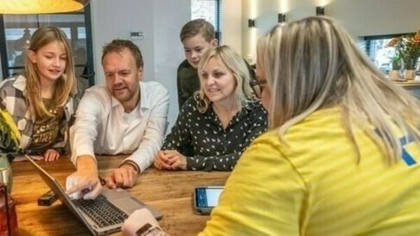 An IKEA co-worker in a yellow shirt sat behind a laptop helping a family.
