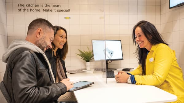 An IKEA co-worker in a yellow shirt talks to two people who are planning a kitchen in the kitchen department. 