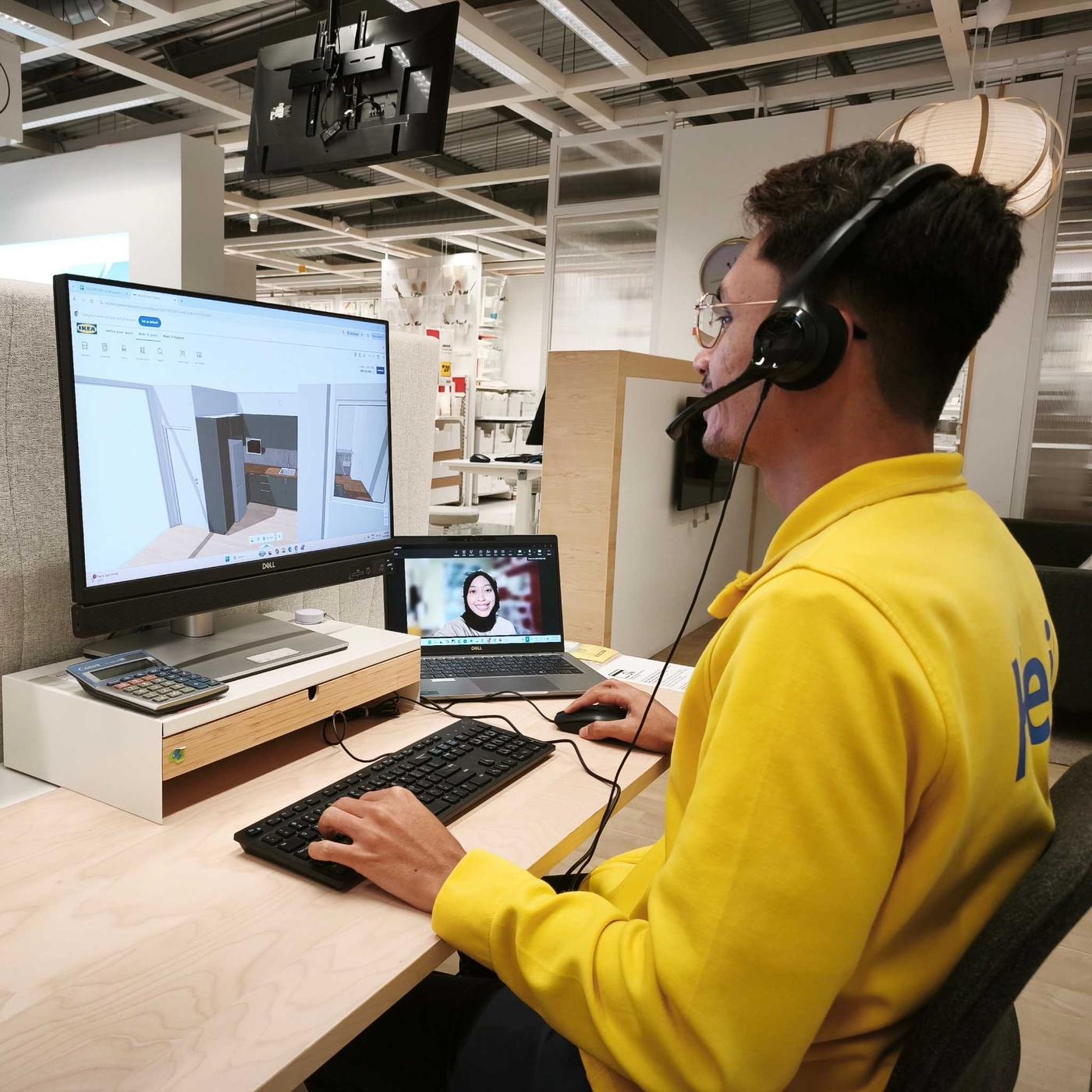 An IKEA co-worker in a yellow sweatshirt and headset uses a desktop computer showing 3D room-planning software while assisting a customer with refreshing her room through a video call.