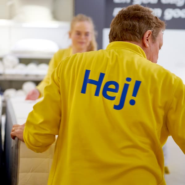 An IKEA co-worker in a yellow uniform with the word “Hej!” in blue on the back.
