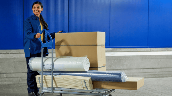 An IKEA co-worker pushes a trolley with IKEA packages and a rolled-up mattress in plastic.