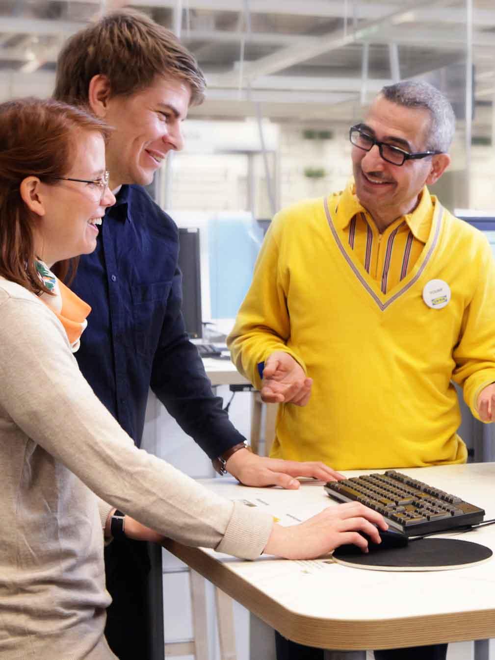 An IKEA co-worker smiling towards a man and a woman in front of a planning system