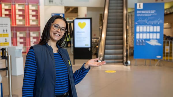 An IKEA co-worker standing in the store entrance lobby giving a welcoming gesture