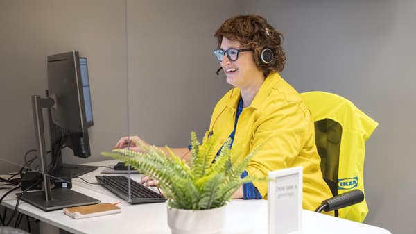 An IKEA co-worker with a headset on smiling at a desktop computer.