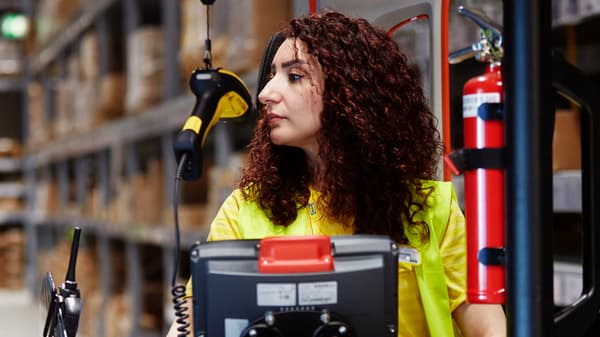 An IKEA co-worker with long dark hair driving a forklift in the self service area.