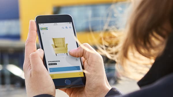 An IKEA customer looking at a yellow STRANDMON armchair on her mobile phone.