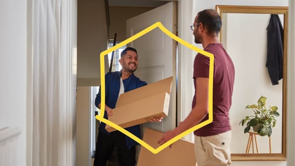 An IKEA delivery person handing over a flatpack box to a customer at their doorstep. A yellow frame in the shape of a hexagon on top of the image.