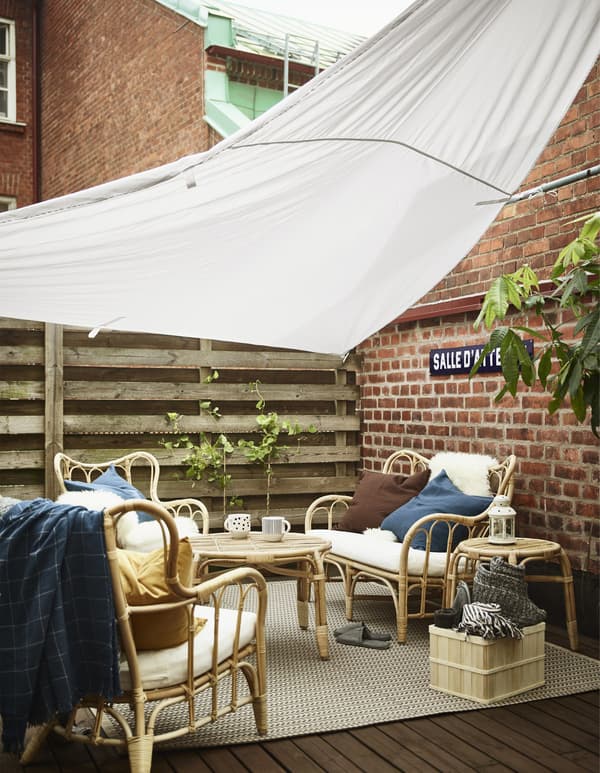 An IKEA DYNING canopy erected over a terrace shields an outdoor sofa, two armchairs and some tables from the sun.