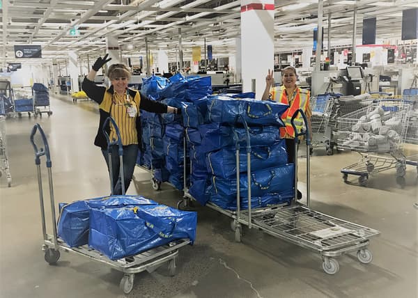 An IKEA employee smiling beside several shopping carts stacked high with blue IKEA bags filled with supplies.
