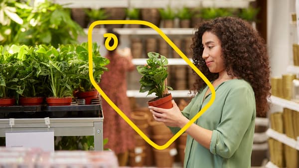 An IKEA Family member holds a plant in an IKEA store.