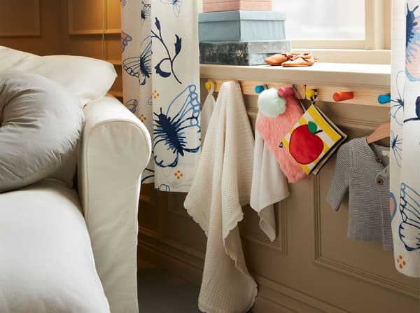 An IKEA FLISAT knob rack with 4 colourful cone-shaped knobs under a window sill with soft toys and baby towels.