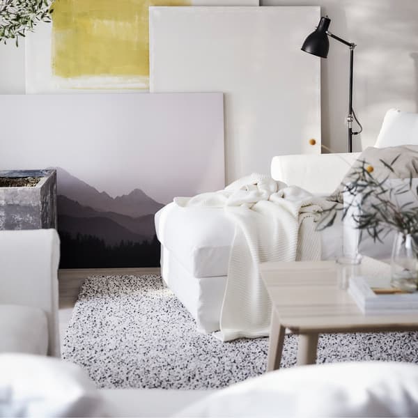 An IKEA GRÖNLID white chaise longue on a dotted carpet, near a wall with artworks propped against it.