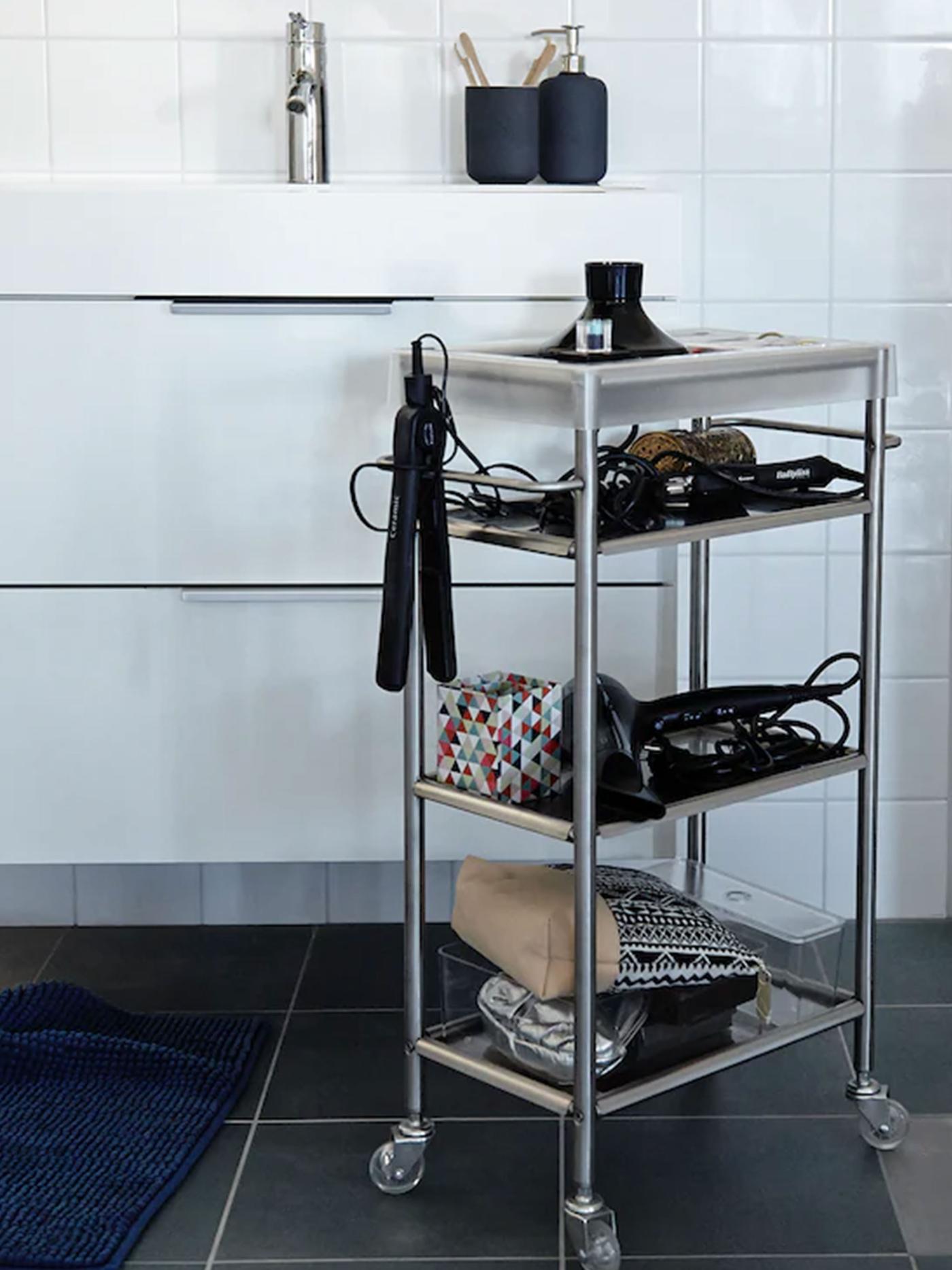 An IKEA GRUNDTAL cart stocked with blowdryers, curling irons, and other accessories stands in front of a bathroom sink.