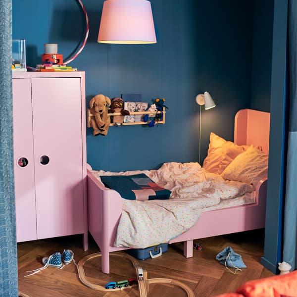 An IKEA HÄLLAN BUSUNGE light pink extendable bed, with a pink wardrobe and a train set on the floor.