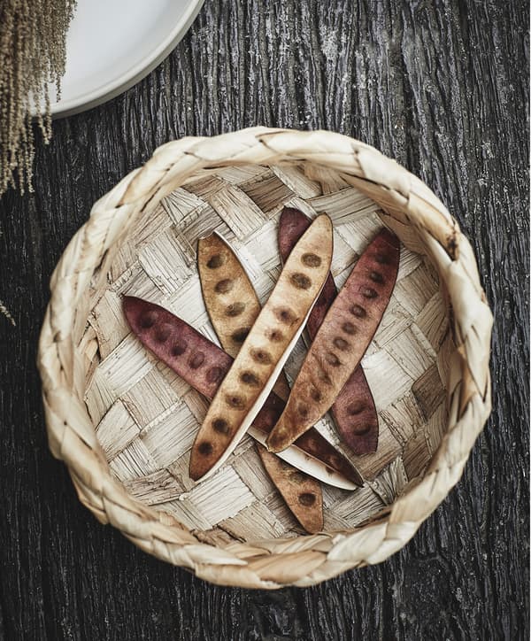 An IKEA HANTVERK basket made with banana fibre seen from above, with several brown, exotic pea pods lying inside.