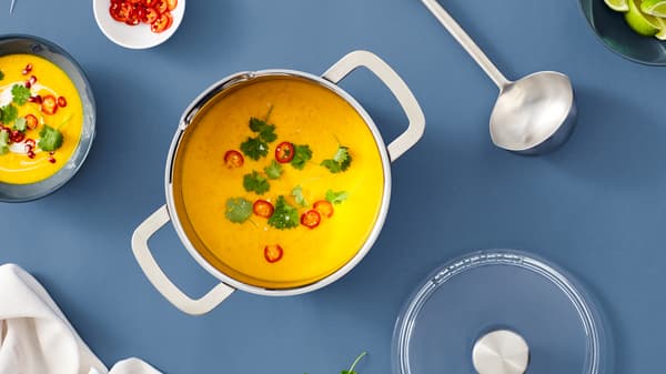 An IKEA HEMKOMST stainless steel pot with soup inside, on a blue surface